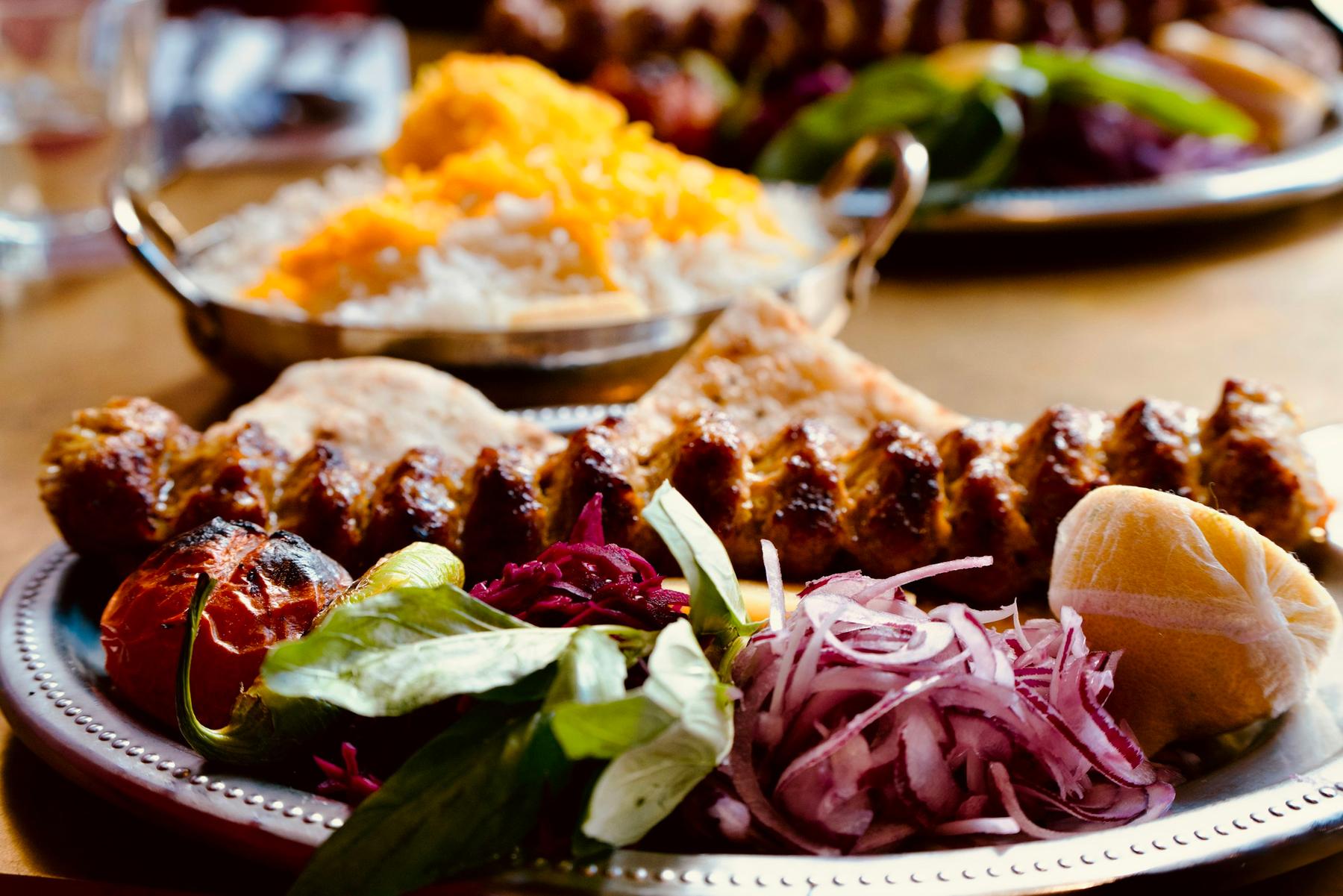 Demo-Foto: gegrillte Kebabspieße mit Fladenbrot, Salat, Zwiebeln und Reis auf einem Metallteller