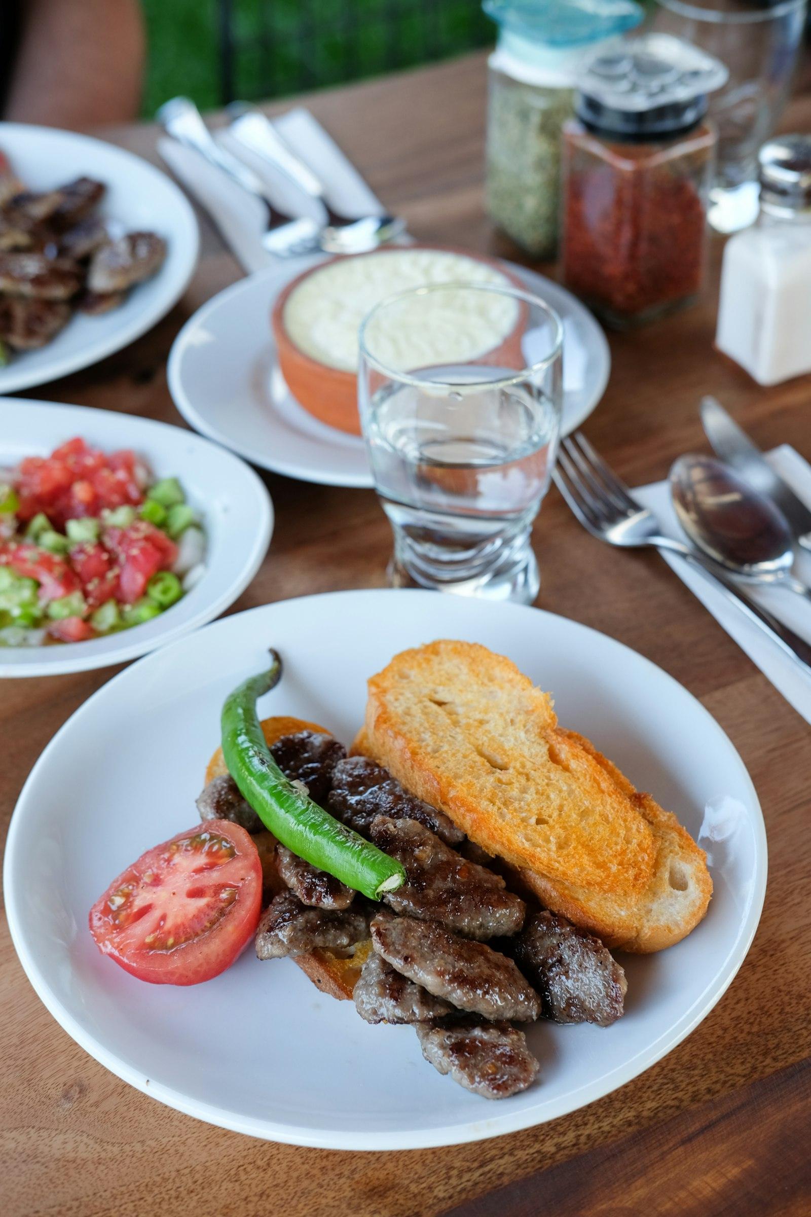 Demo-Foto: Teller mit gegrilltem Fleisch, Brot, Tomate und grüner Peperoni