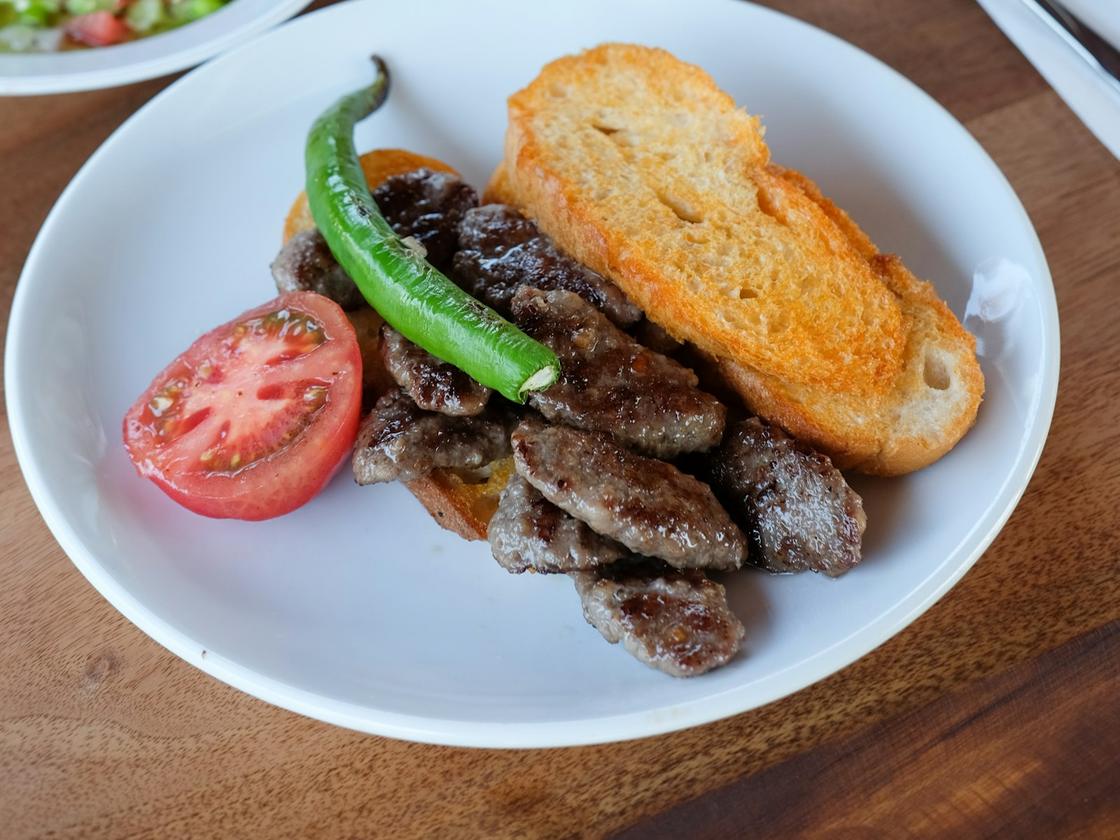 Demo-Foto: Teller mit gegrilltem Fleisch, Brot, Tomate und grüner Peperoni